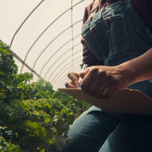 woman in a greenhouse with a clipboard and pen